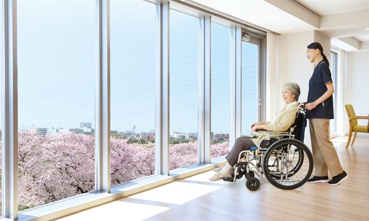 東急ウェリナケア尾山台のスカイリビングから多摩川沿いの桜並木を眺める入居者とスタッフ
