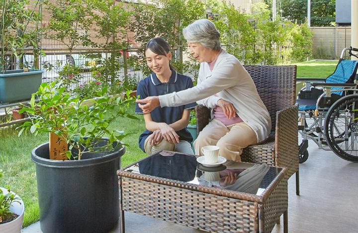 東急ウェリナケア旗の台の中庭のテラス。入居者とスタッフが植栽を眺めるようす