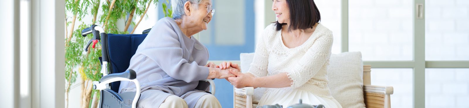 車いすに座る高齢の女性と、手を握って話す娘