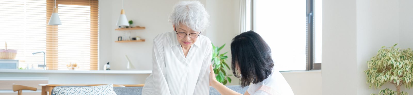 明るいリビングで、ソファから立ち上がる高齢の女性を支える女性