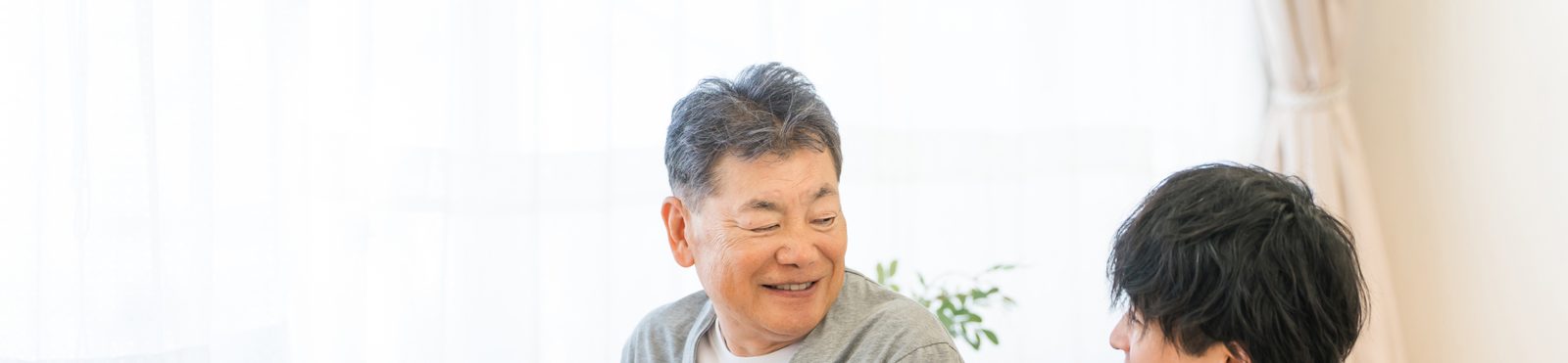 車いすに座る高齢の男性と、そばにしゃがんで話しかける介護スタッフ