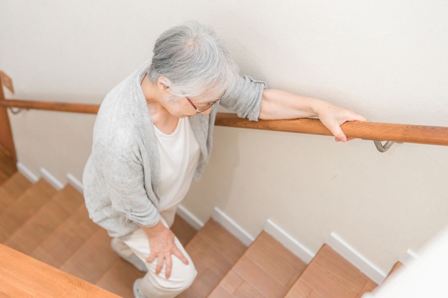 手すりにつかまりながら、階段を上る高齢の女性