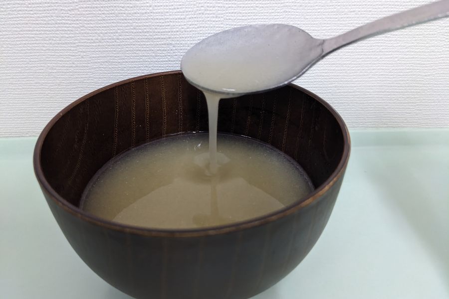 薄いとろみをつけたみそ汁を、スプーンですくって流すようす。細く流れ落ちる