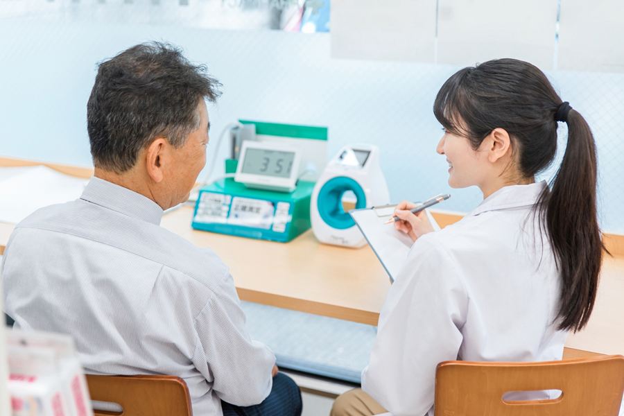 健康診断で、高齢の男性の話を聞いて記録する医療スタッフ