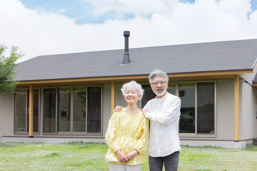 住宅の前に並んで立つ、笑顔の高齢の夫婦