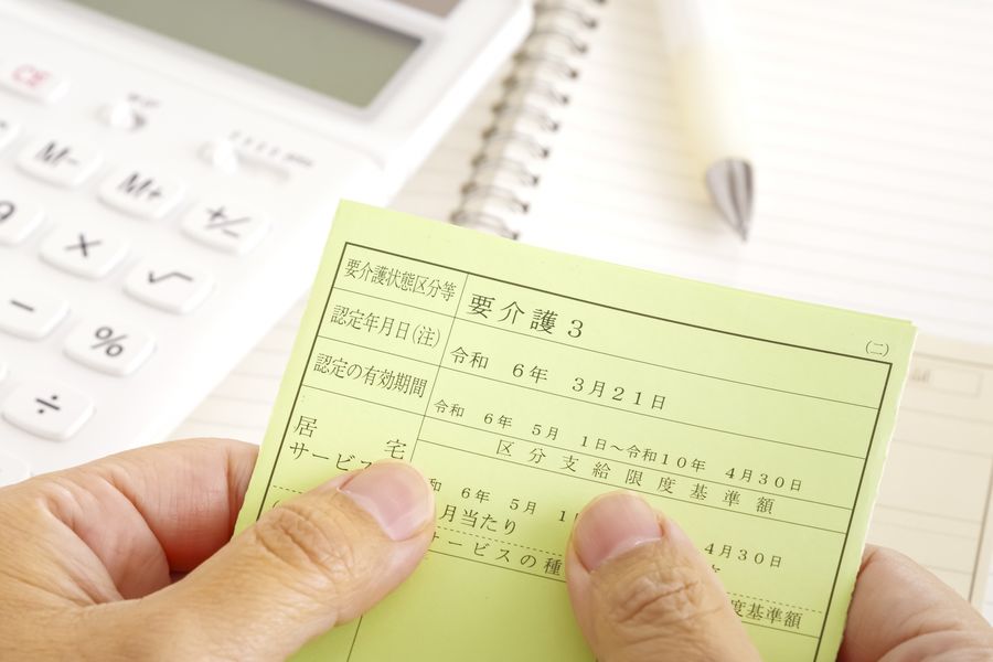「要介護3」と書かれた介護保険の被保険者証を持つ手元と、電卓