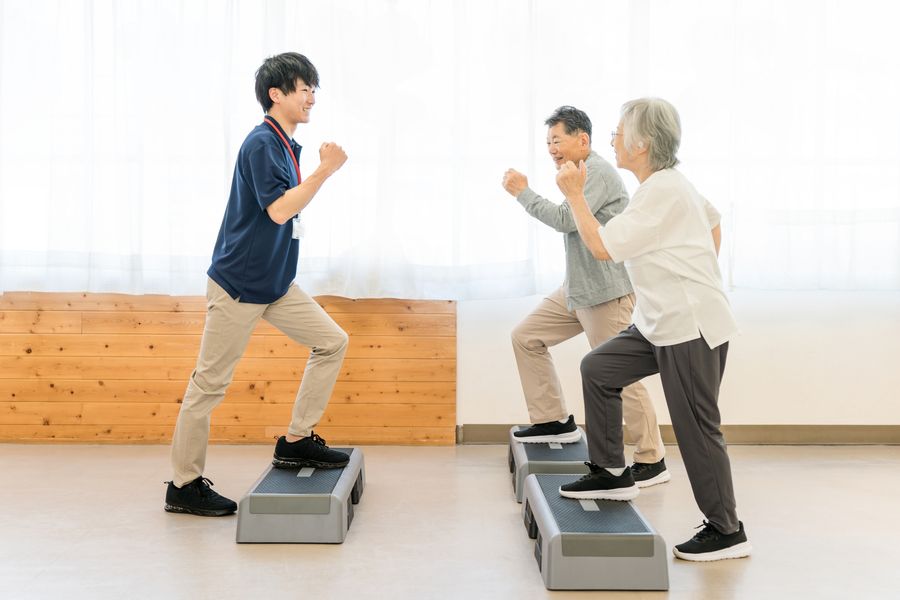 踏み台を使って、スタッフと一緒に運動する高齢の男女