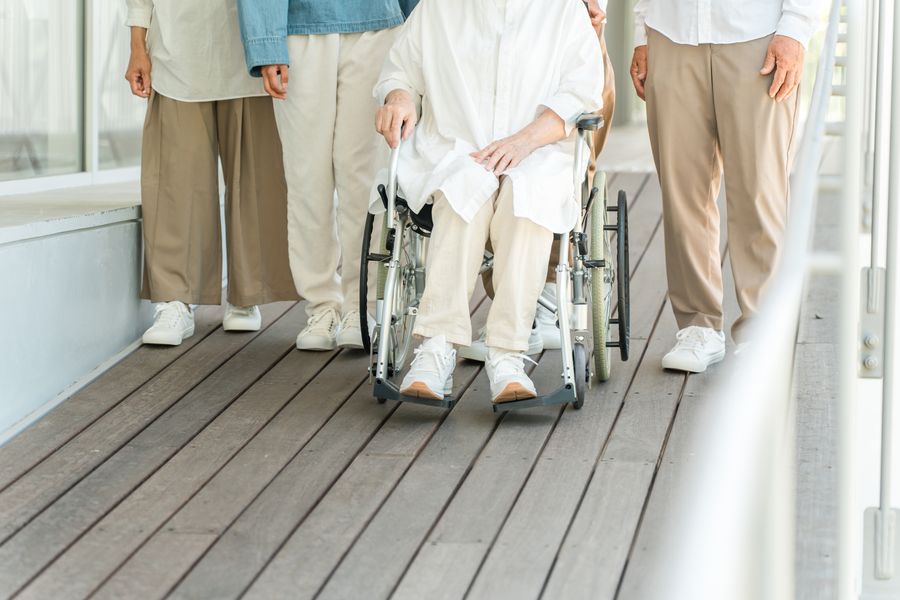 木の床の通路で、車いすの方に付き添って歩く家族の足元