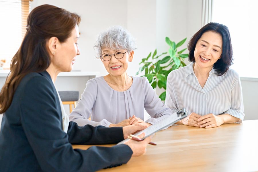 書類を示しながら、高齢の母と娘に説明する相談員