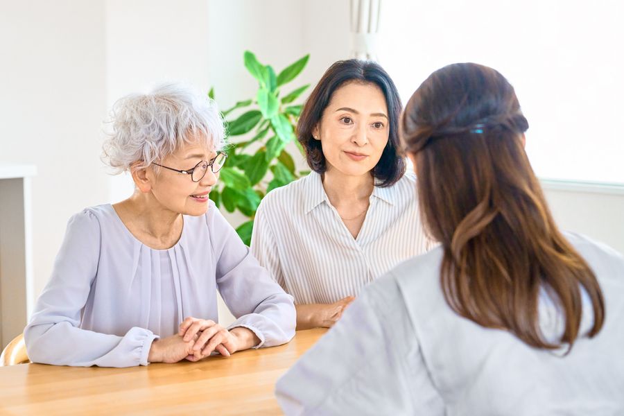 テーブルをはさんで、職員の話を聞く高齢の女性と家族