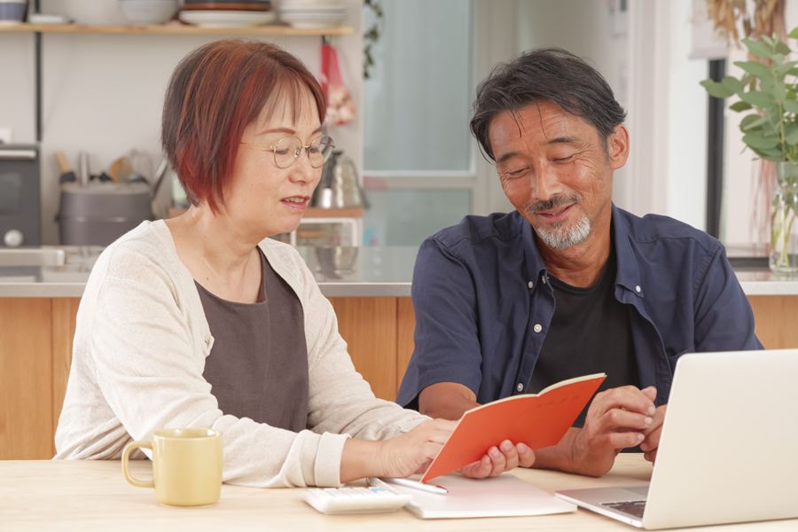 手帳とノートパソコンを見ながら話し合う高齢の夫婦