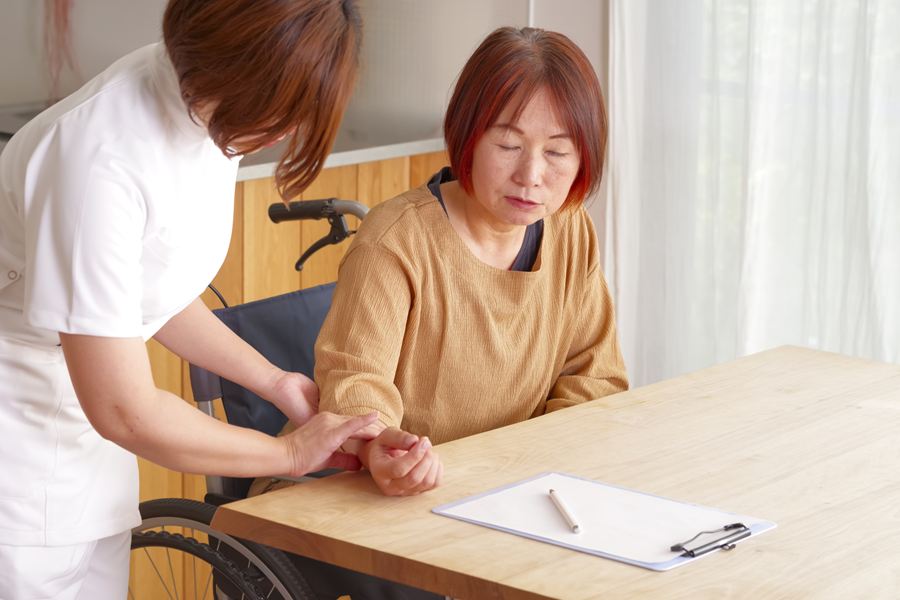 車いすの女性の腕をとり、脈を確かめる看護スタッフ
