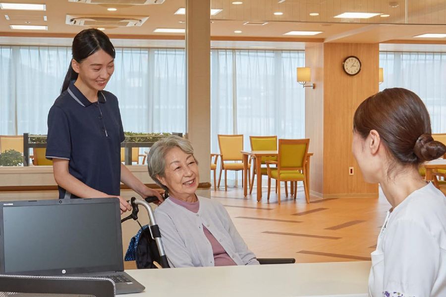 共用スペースで、車いすの入居者に付き添うスタッフ