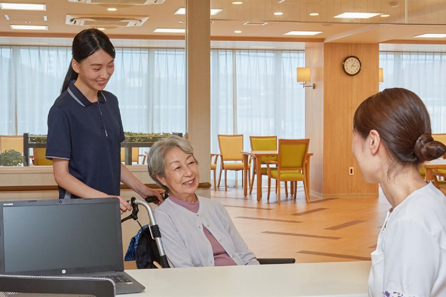 窓の大きなダイニングで、車いすのご入居者に声をかけるスタッフ