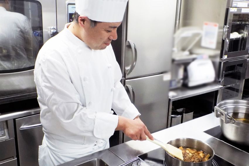 尾山台の厨房で、鍋の煮込み料理を調理する調理師
