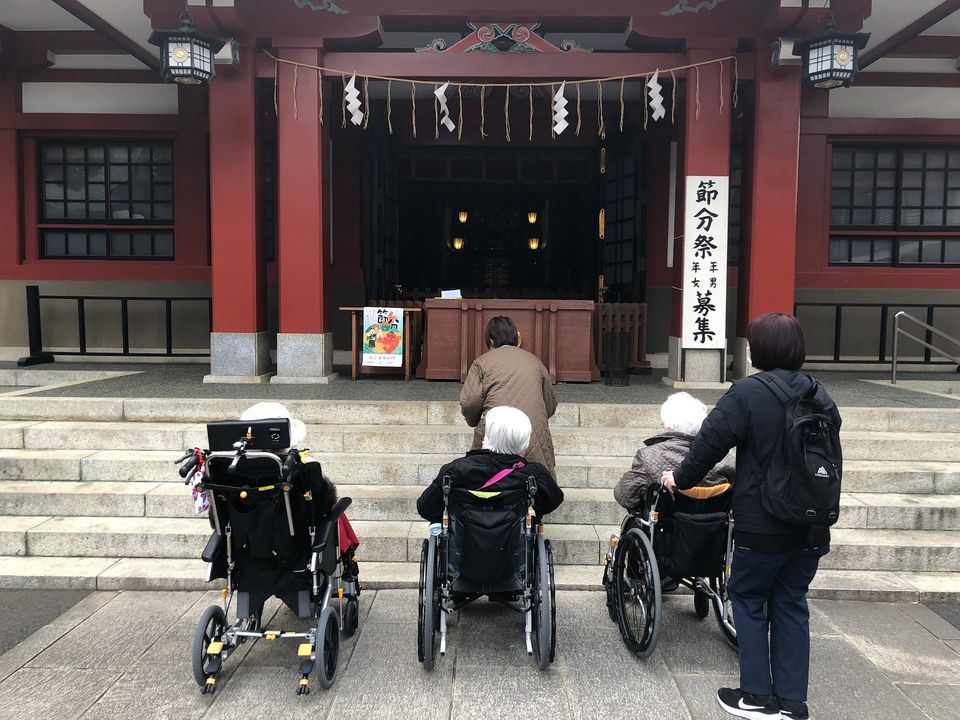 旗岡八幡神社の拝殿の前で、車いすのご入居者とスタッフがお参りする様子