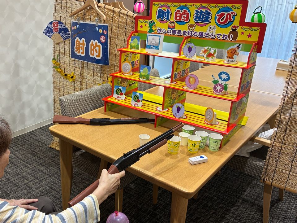 納涼祭の射的の屋台で、おもちゃの銃をかまえるご入居者